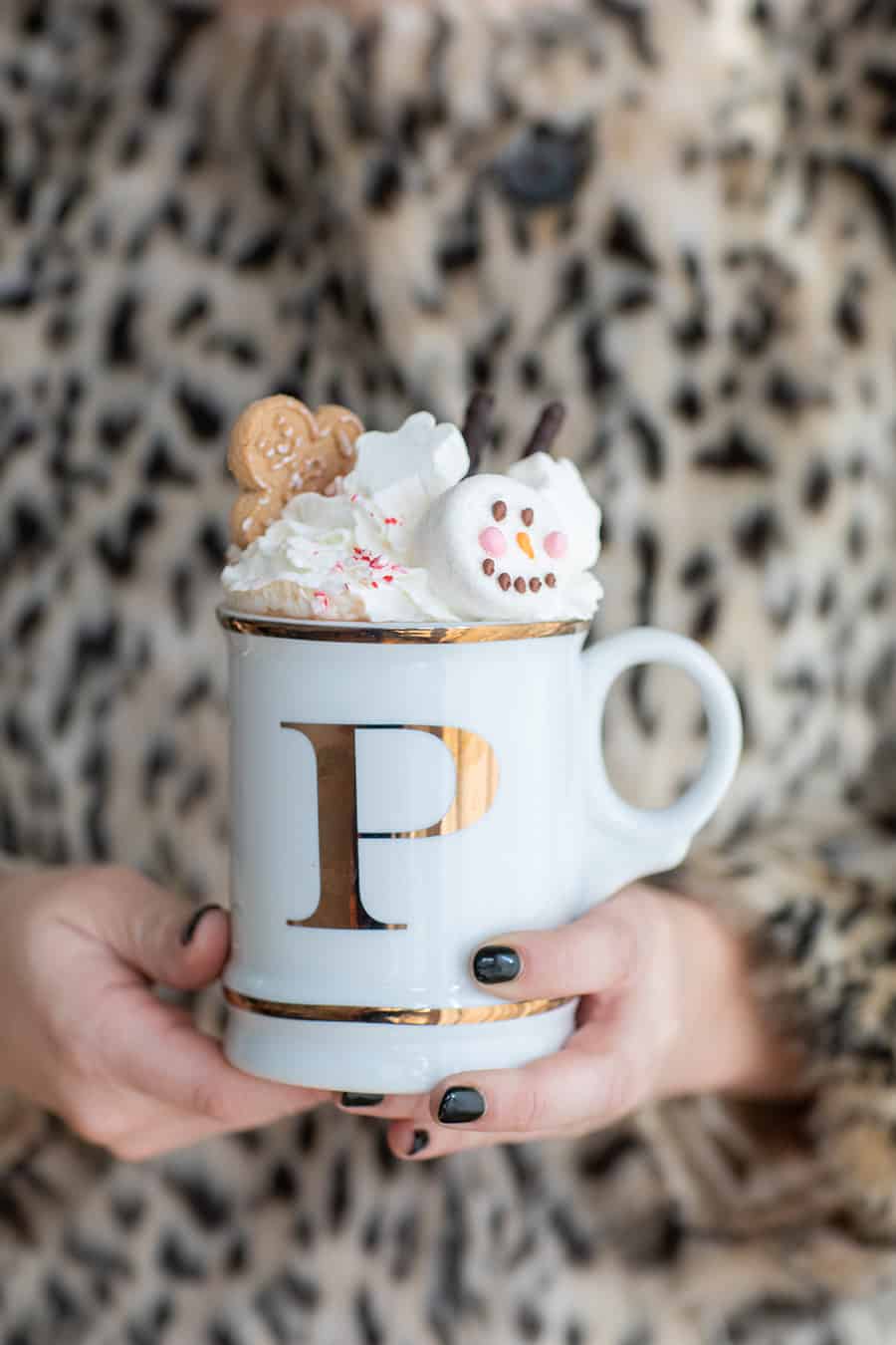 Girl holding a mug of hot chocolate topped with whipped cream, cookies and marshmallow. 