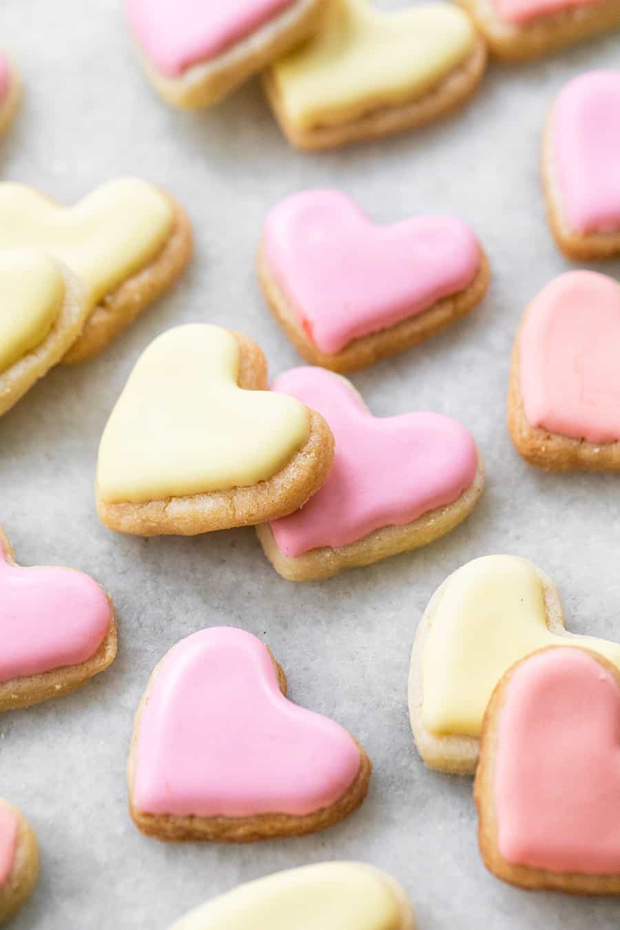 mini heart shaped sugar cookies in yellow and pink on a marble table 
