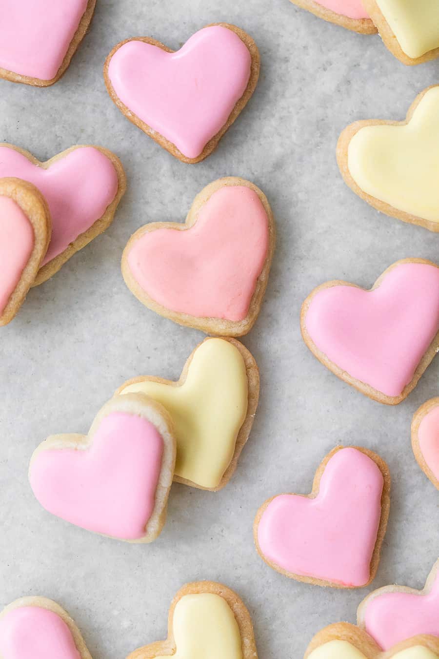 mini heart shaped sugar cookies frosting in pink and yellow royal icing on a marble table. 