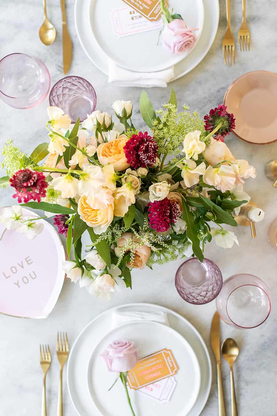 Romantic flowers in the center of a table with pink, white and gold dishes. 