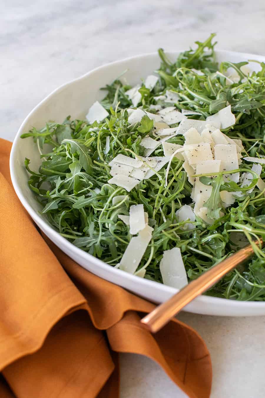 simple arugula salad with parmesan on top, gold spoon and yellow napkin.