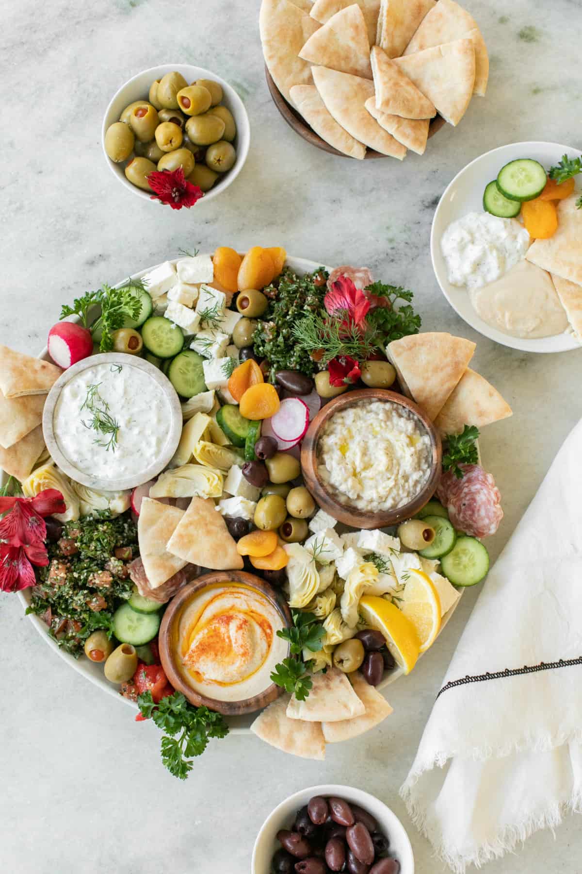 Plato de comida griega con aceitunas, hummus, pepinos, limones y pan de pita.