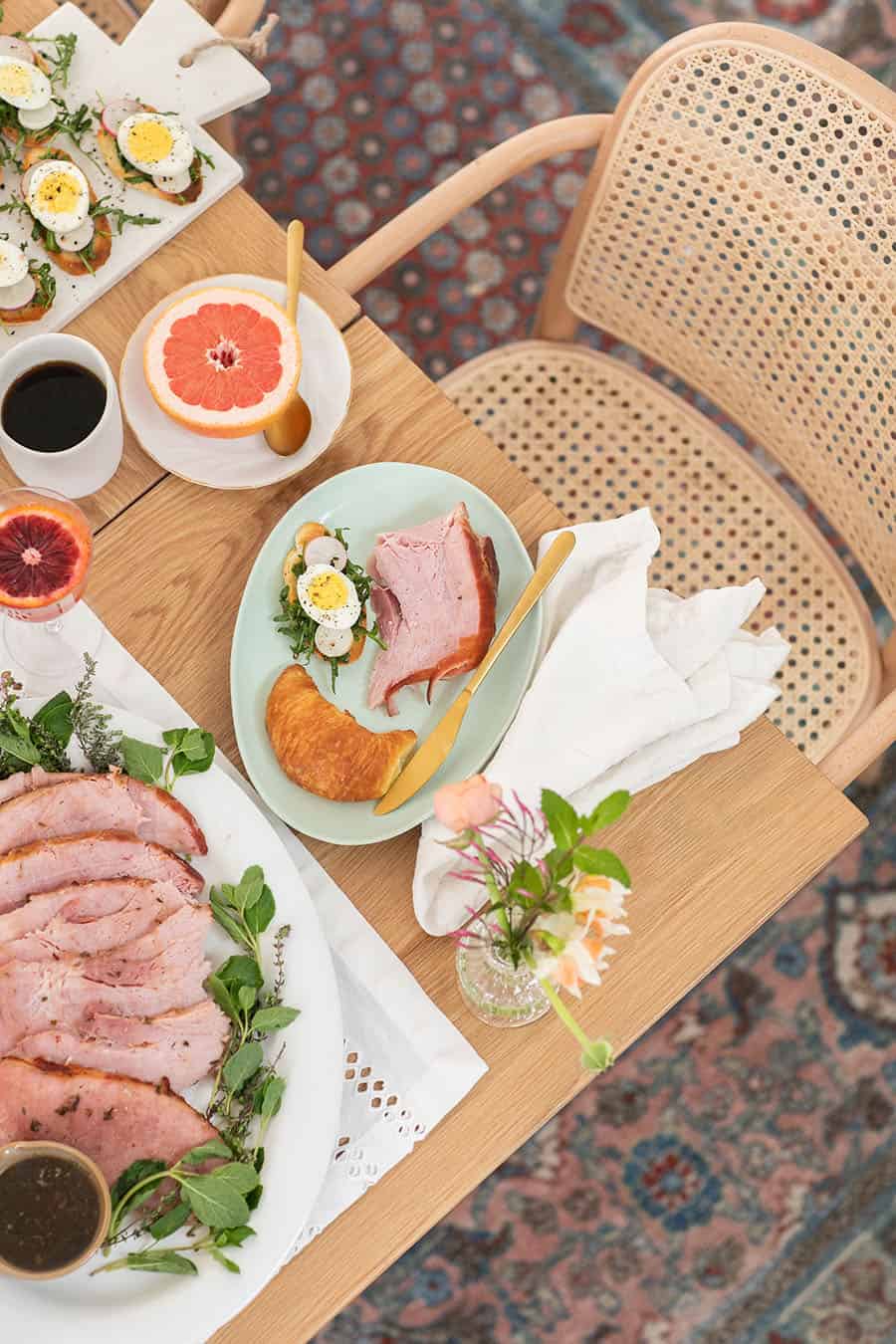 Overhead of an Easter brunch table setting with ham and food.