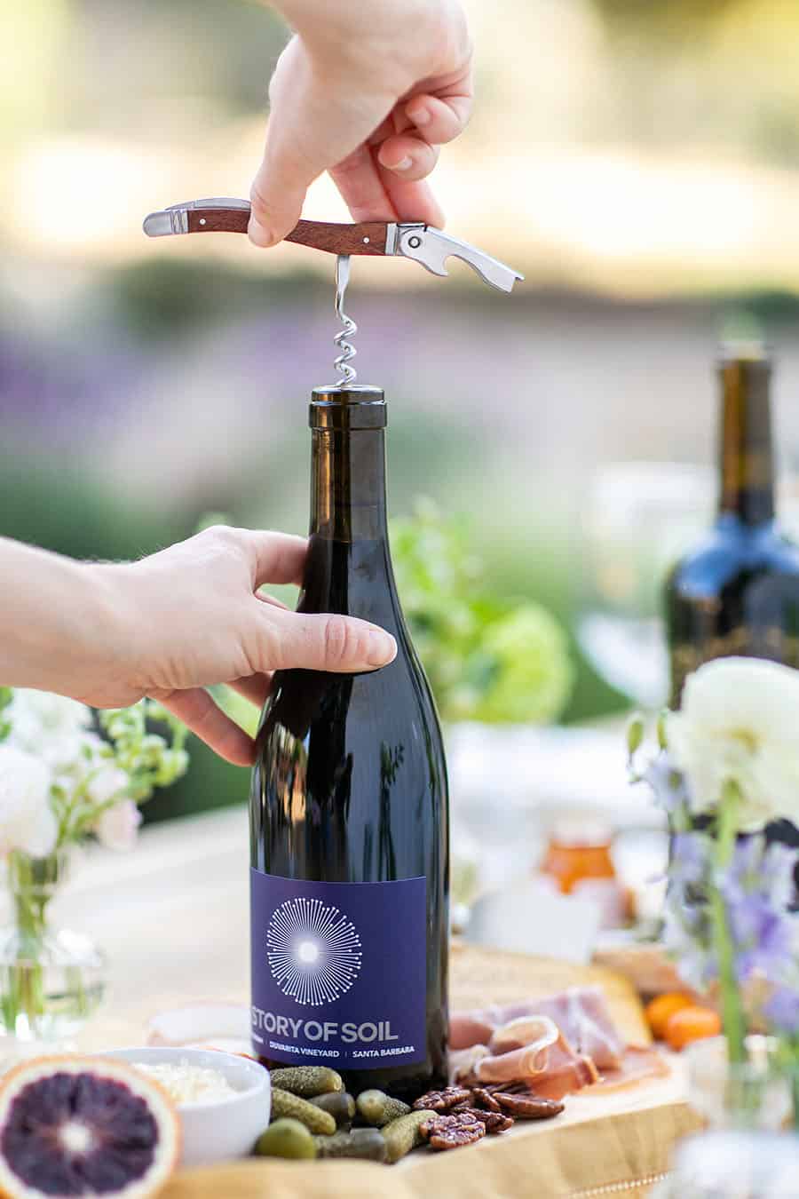 Hand opening a wine bottle with a corkscrew opener.