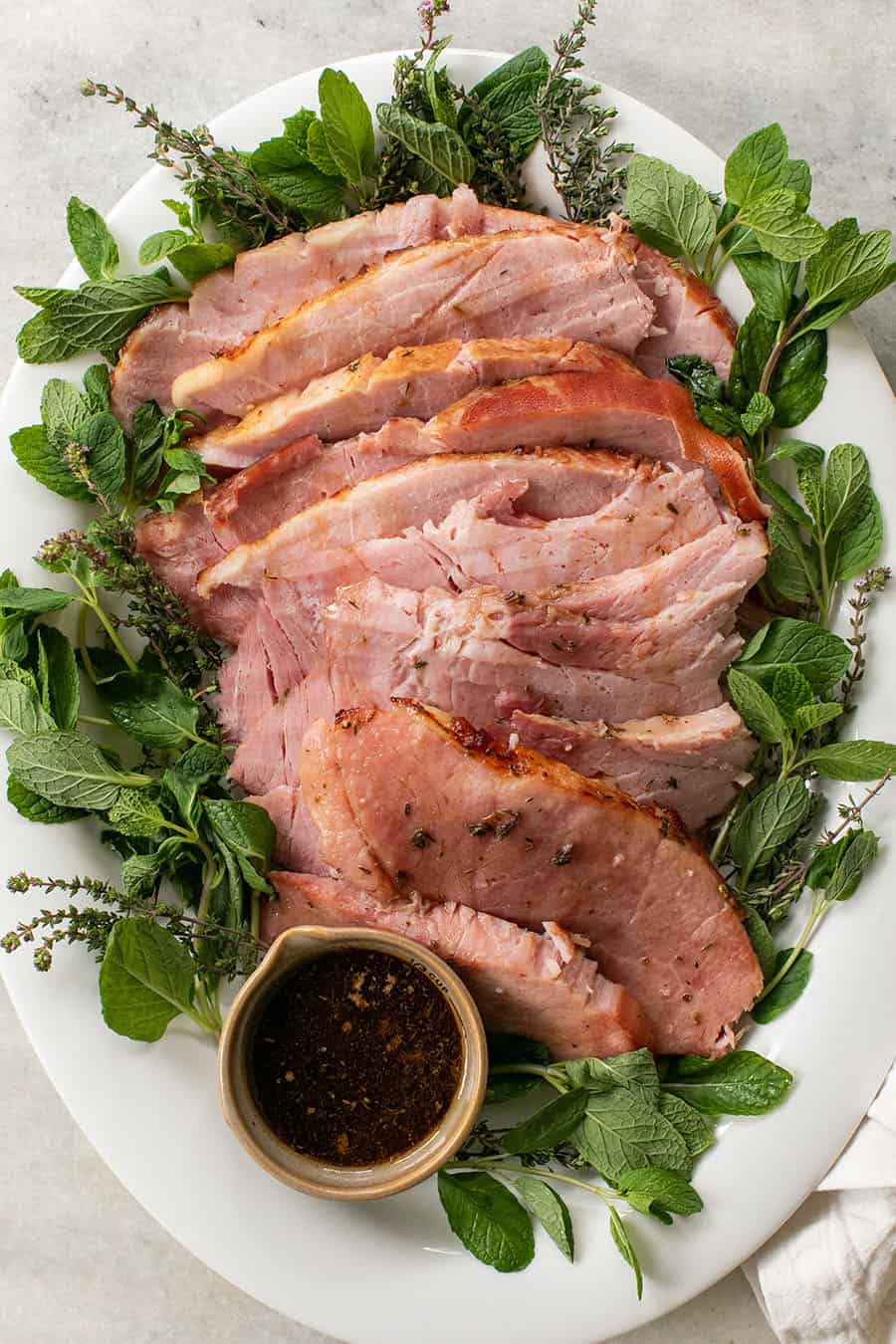 Honey glazed ham sliced on a platter with greens and sauce.