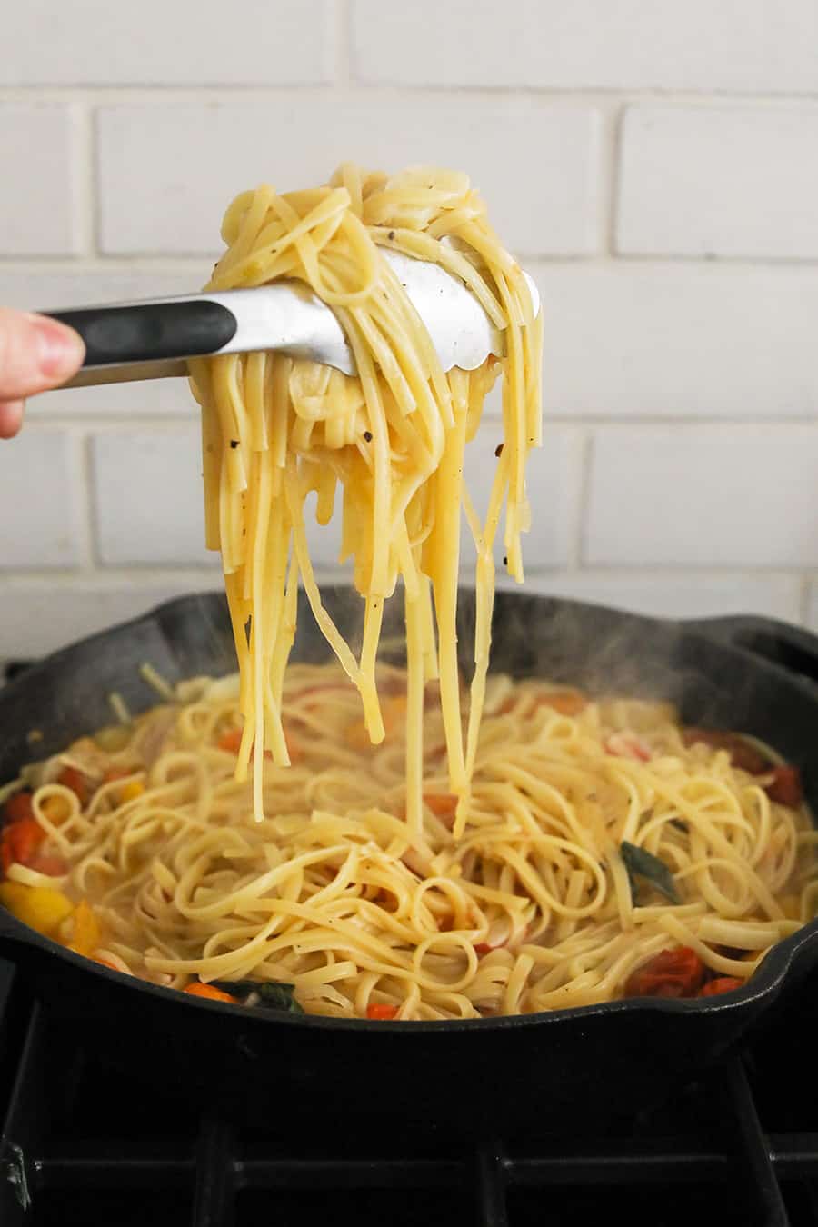 Holding noodles above a cast iron skillet - tomato basil pasta