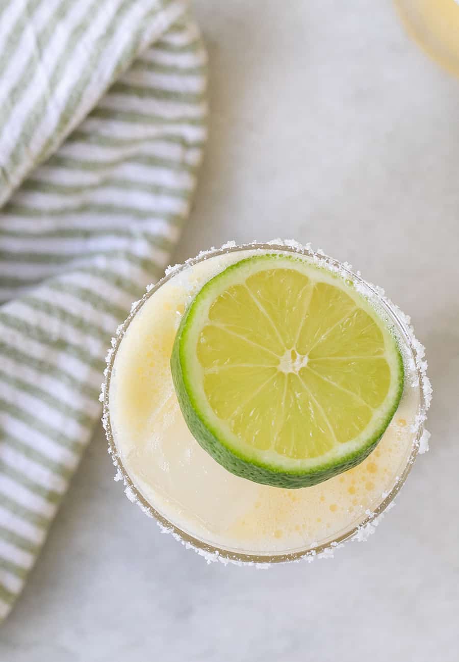 Overhead photo of a skinny margarita with a lime wedge on a marble table. 