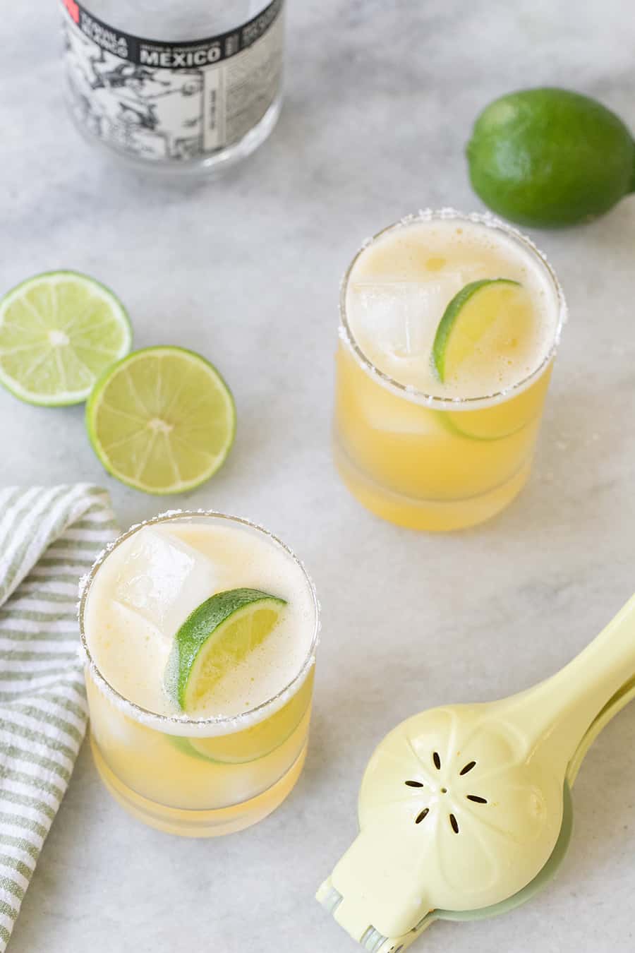 Margaritas with lime wedges on a marble table.