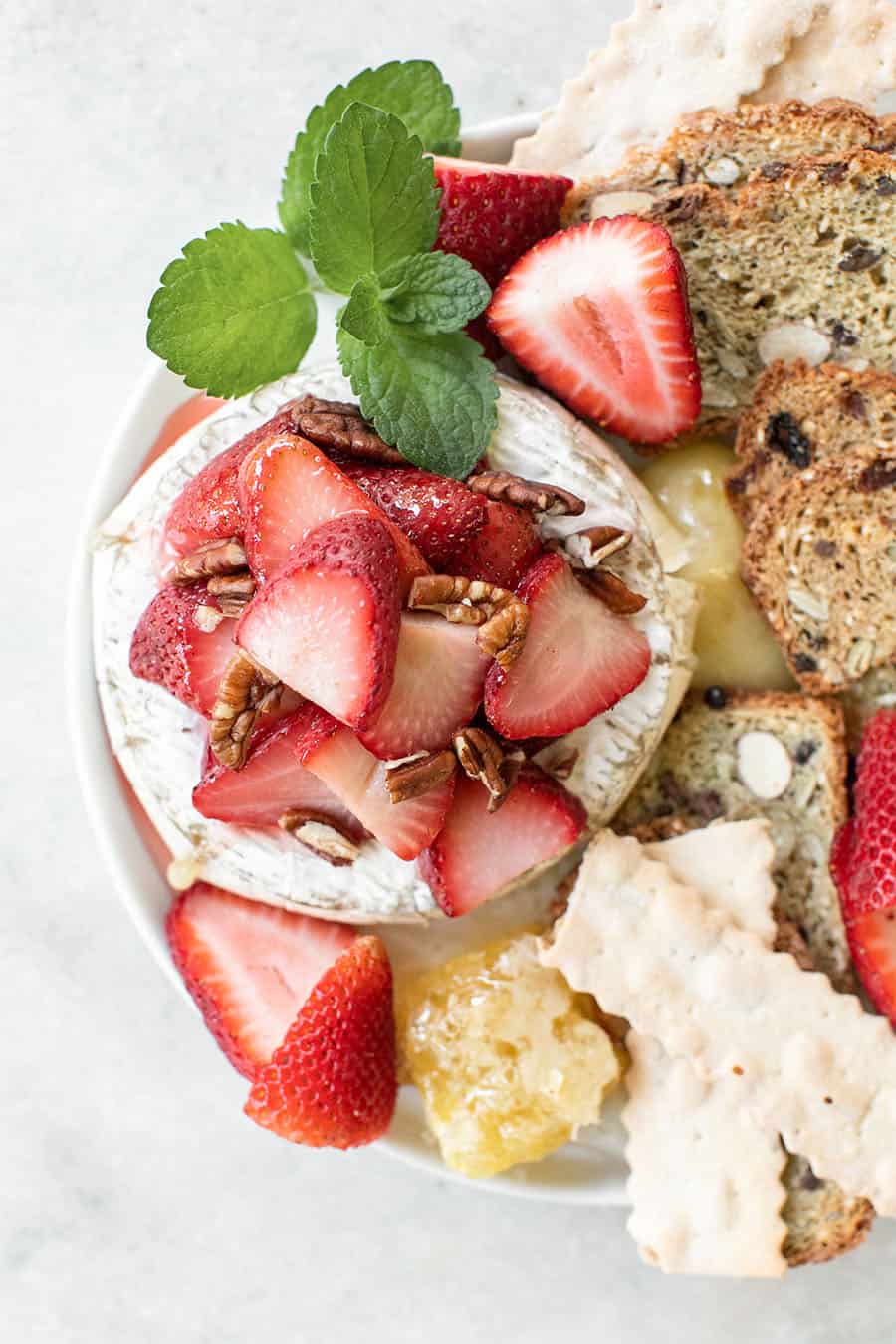 Strawberries topped on melted brie with crackers and honey.