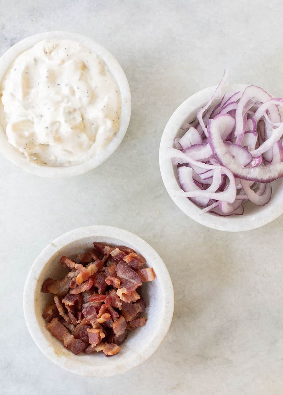 Bacon, blue cheese dressing and onions in marble bowls for a classic wedge salad.