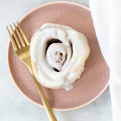 One cinnamon rolls on a pink plate with gold fork.