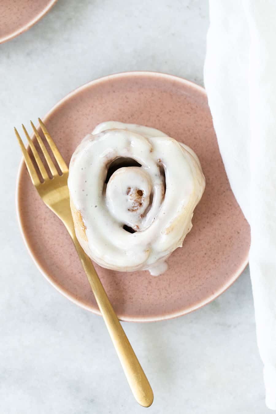 Cinnamon roll on a pink plate with gold fork.