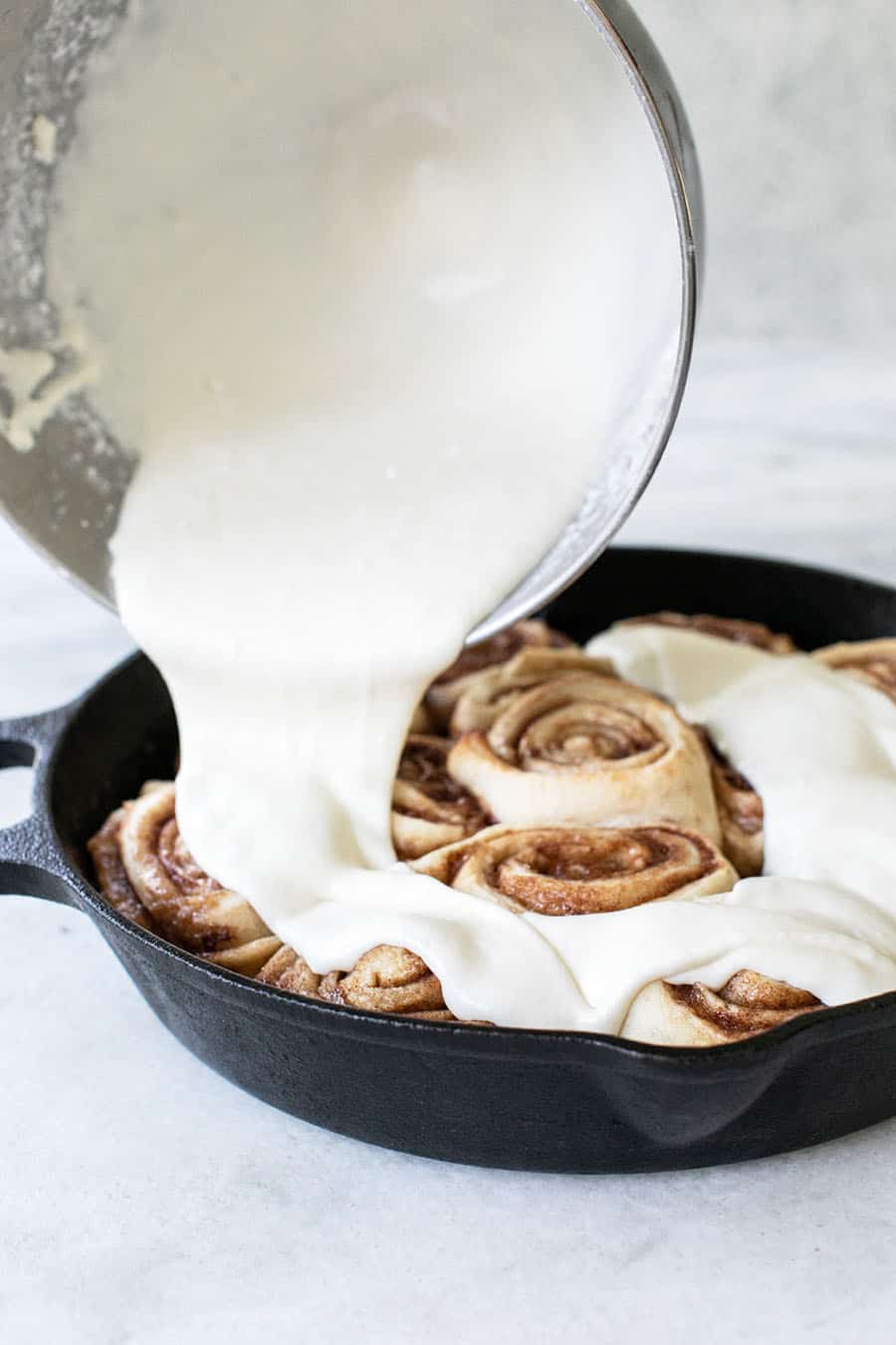 Homemade cream cheese glaze being poured over baked cinnamon rolls.
