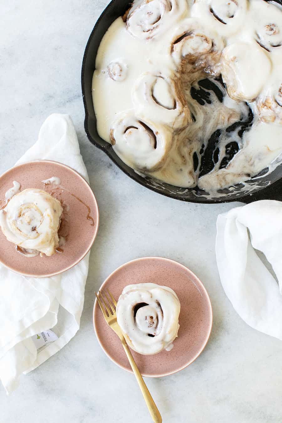 Cinnamon rolls in a cast iron skillet and two on a pink plate.