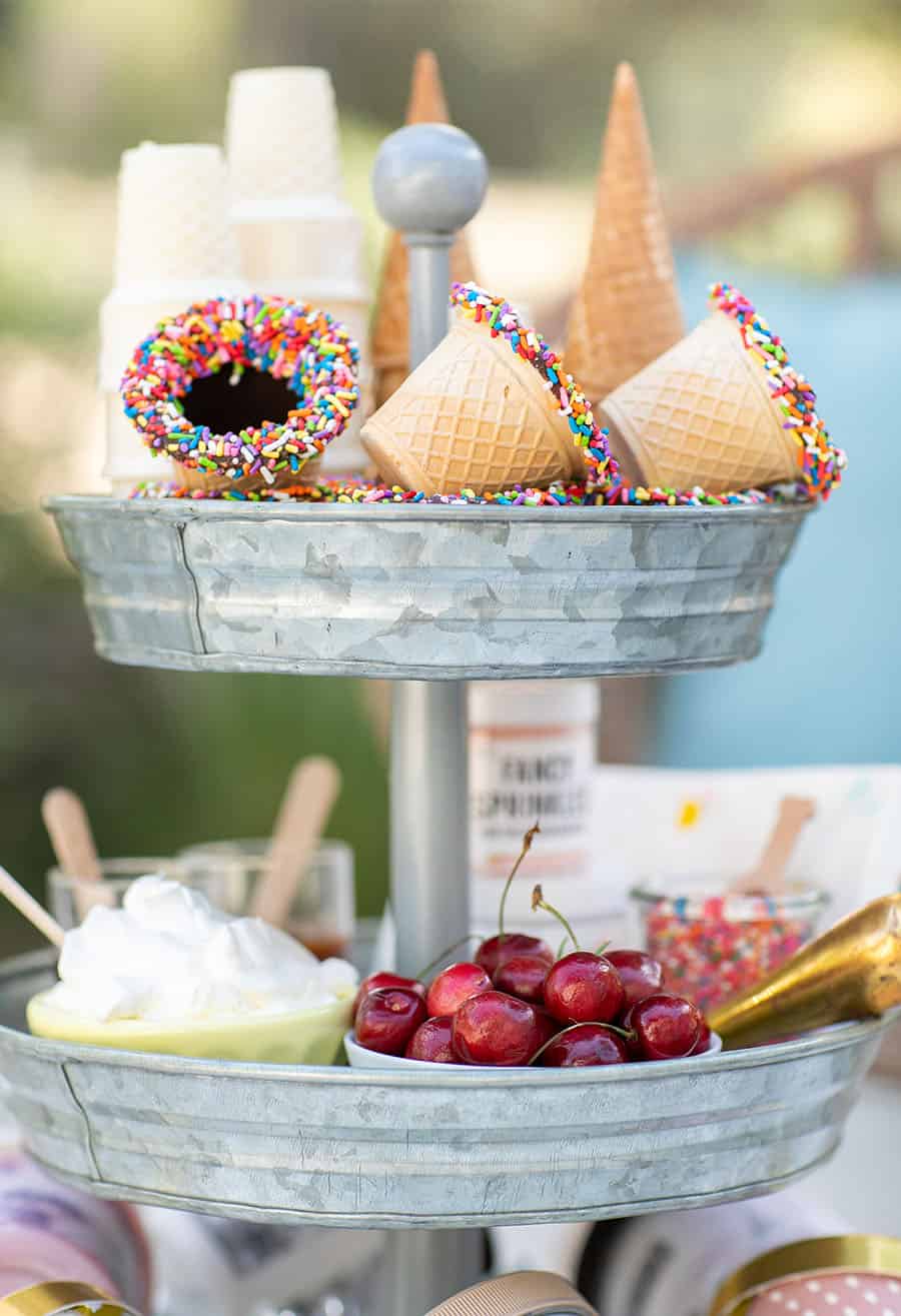 Tiered Galvanized Tray with ice cream cone bowls with sprinkles and cherries in white bowl with whipped cream in yellow bowl.