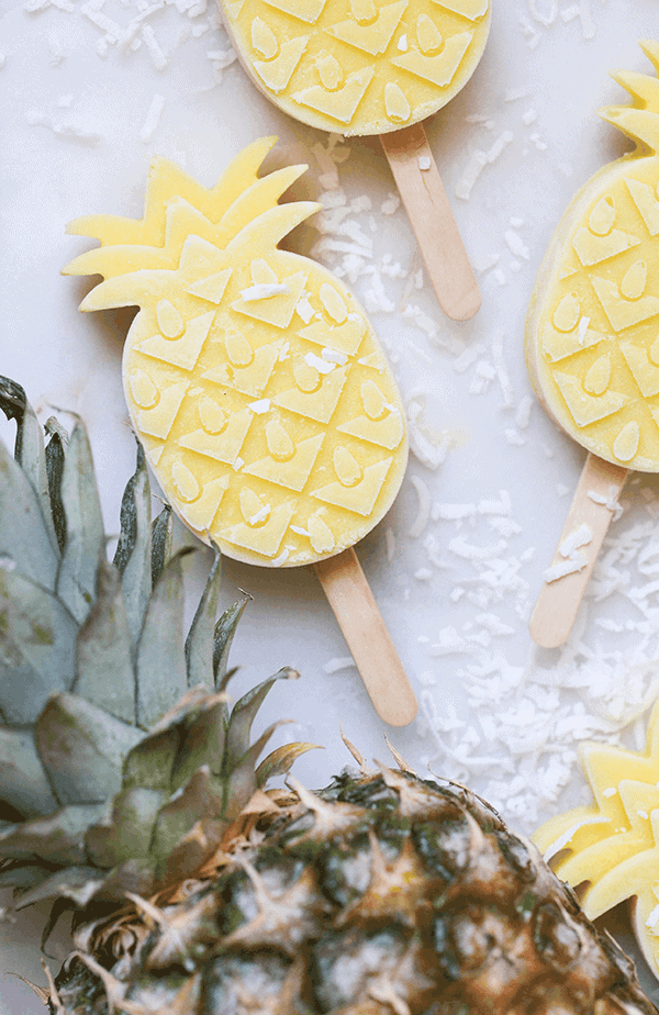 Pineapple shaped popsicles with rum and coconut on table with real pineapple