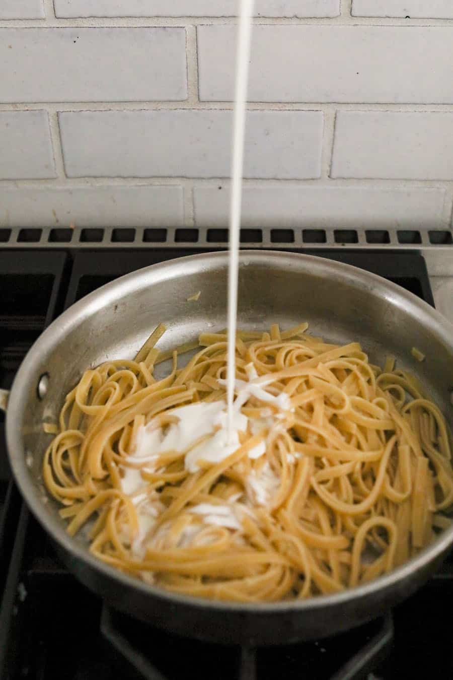 cream being poured over fettuccini noodles in a pan