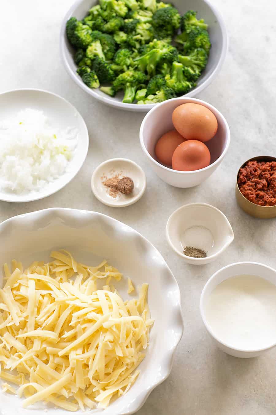 Cheese, eggs, onions, broccoli and spices in small bowls.