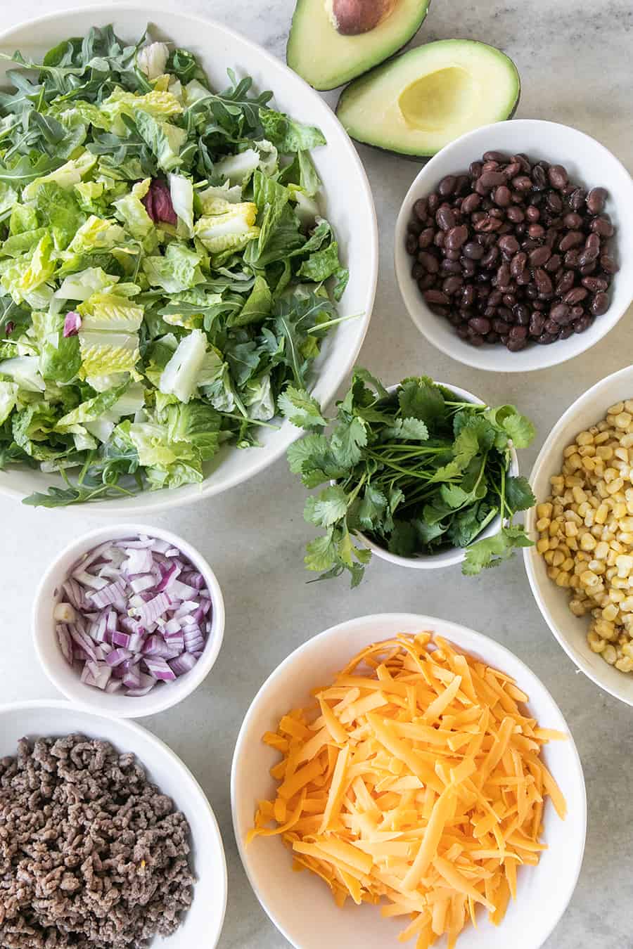 Ingredients for a taco salad, lettuce, onions, cheese, beans, ground beef, corn. 