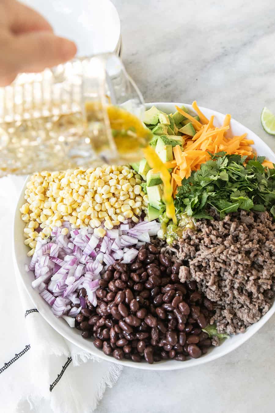 Dressing being poured over ground beef, beans, cheese, corn and onions