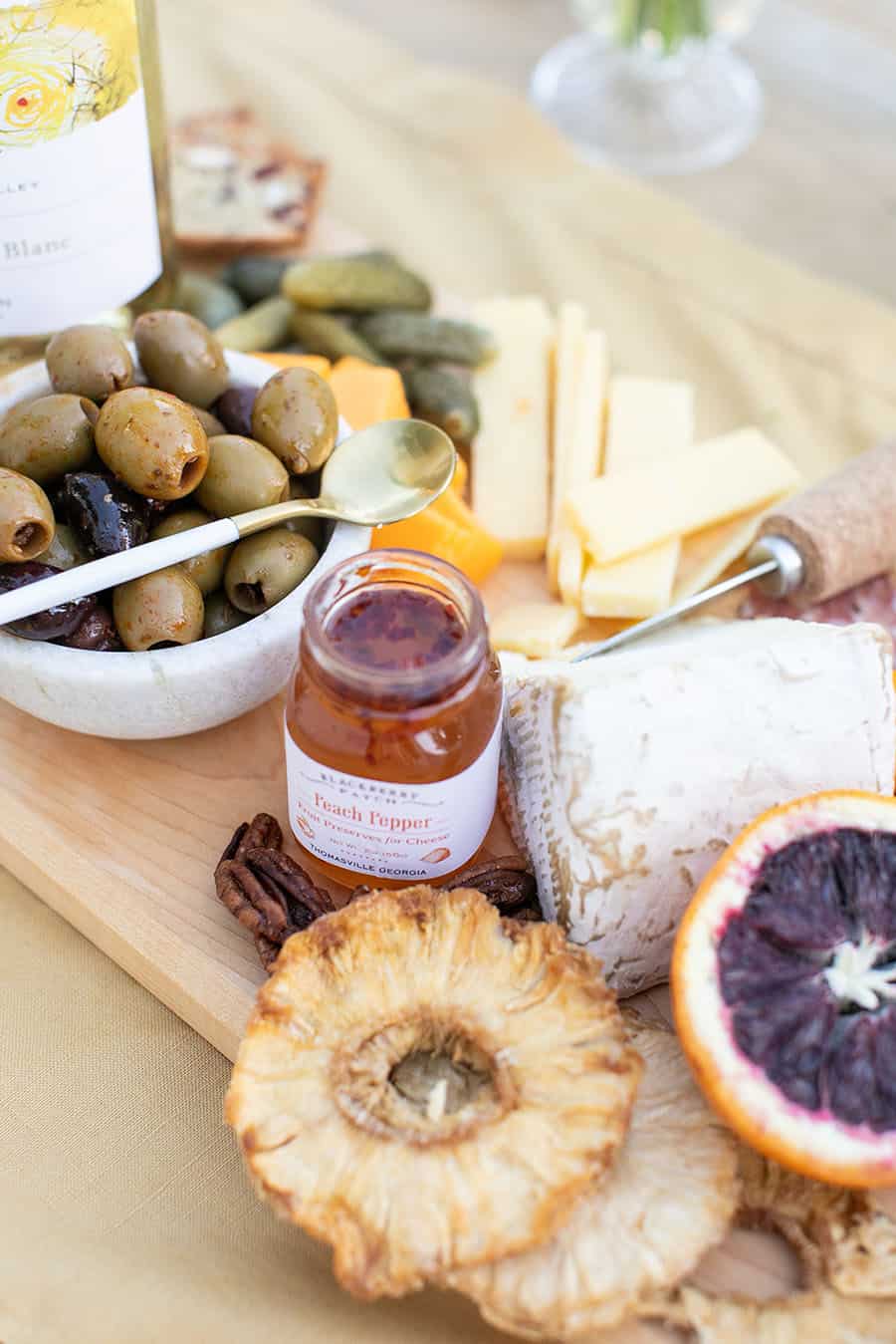 Close up of peach and pepper jam with pineapple rounds and blood orange and olives on a cheese board. 