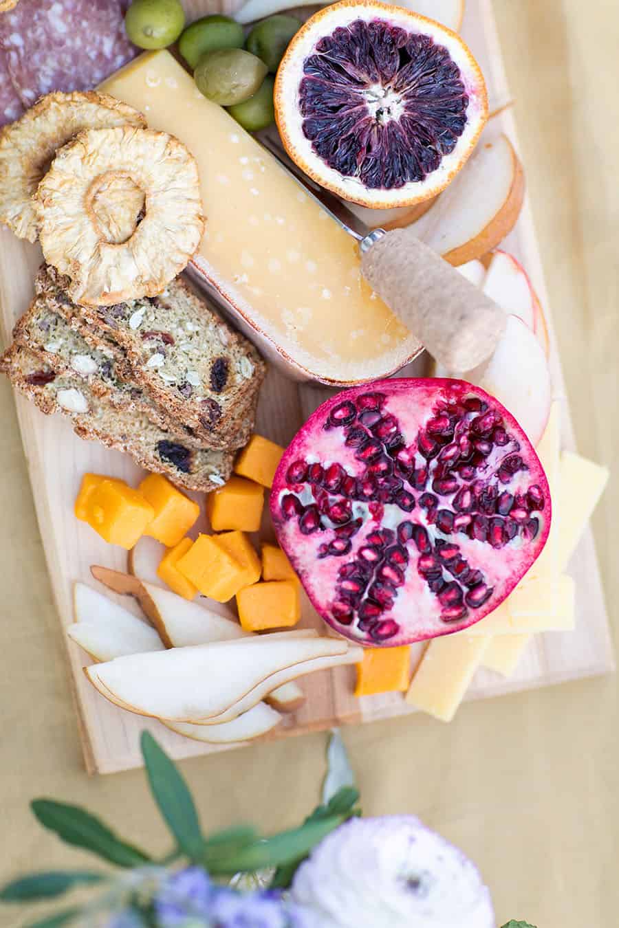 Cut open pomegranate with cheese and pears on a cheese board.