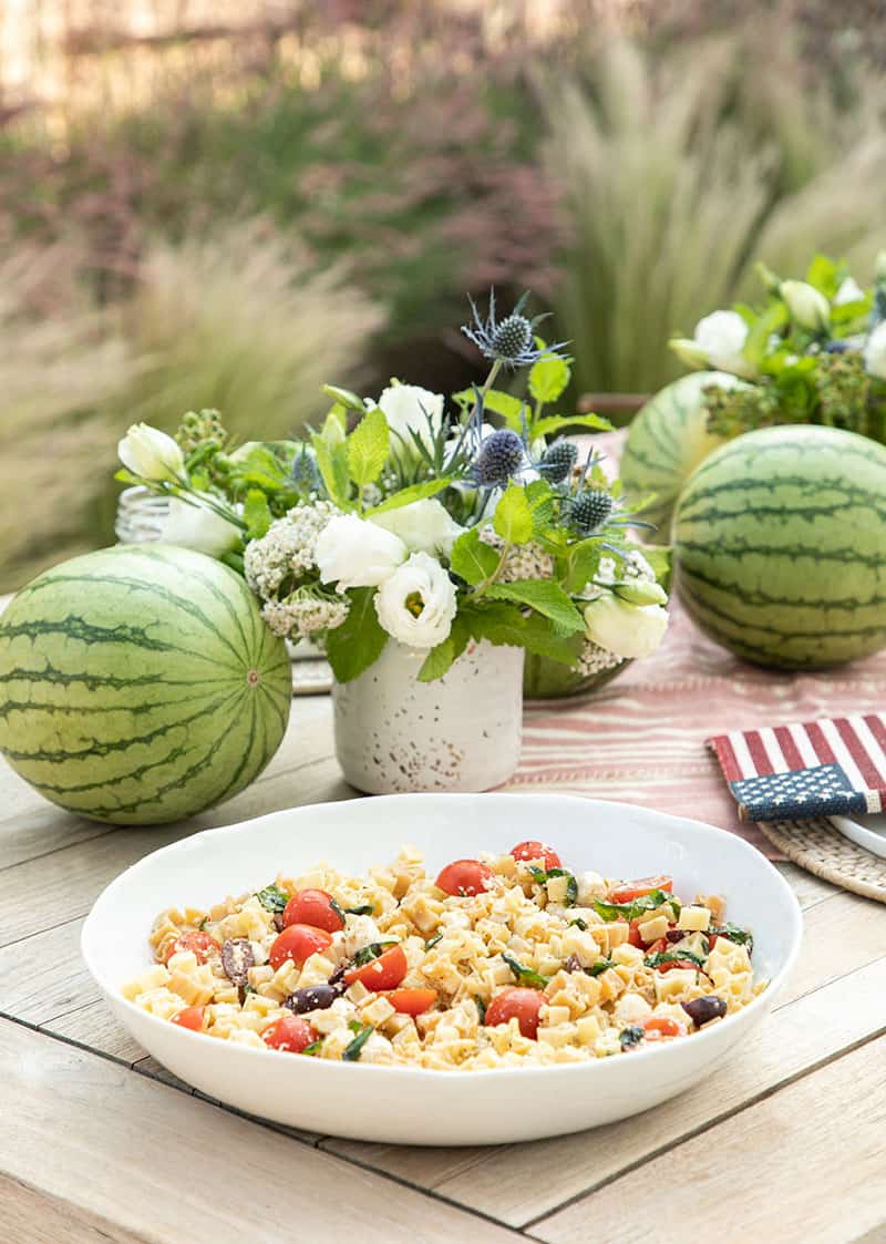 Pasta salad on a table with watermelons and a flower arrangement  