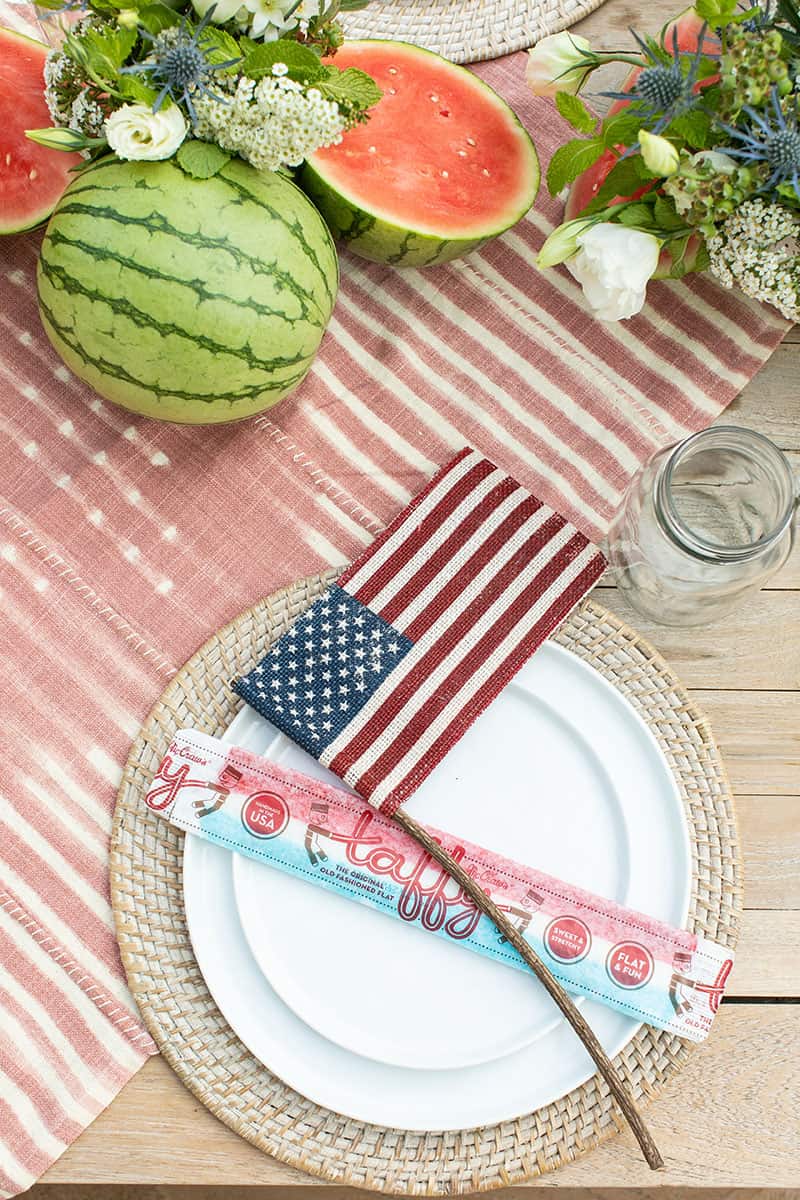 4th of July party table setting with white plates on a woven charger and a burlap flag.