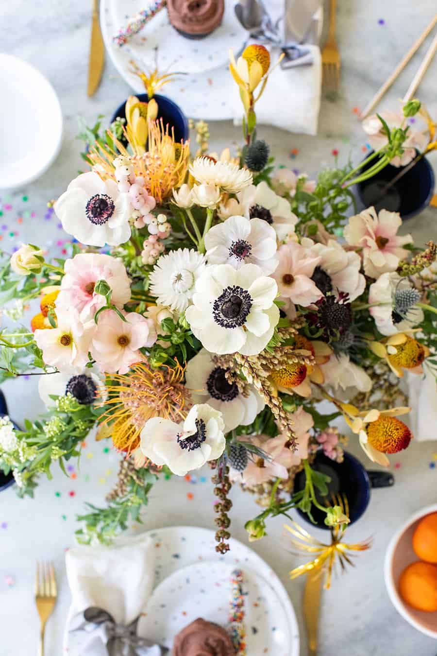 Beautiful floral arrangement on a marble table with plates and cupcakes. 