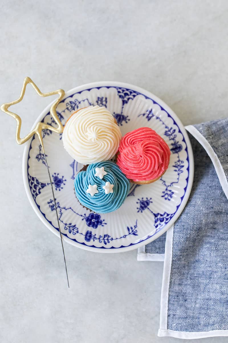 three mini red, white and blue cupcakes on a blue plate with a star sparkler.