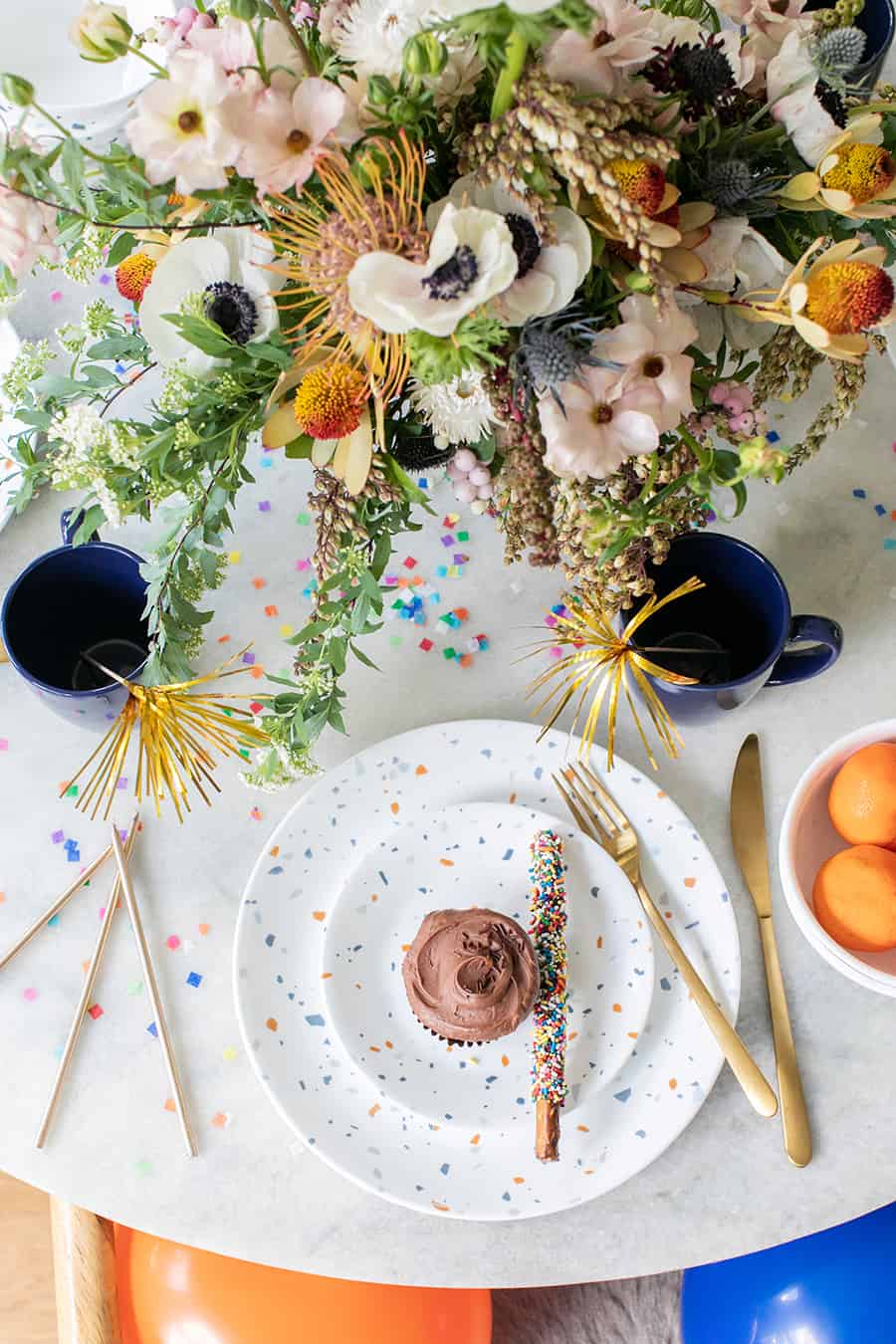 A birthday party set-up with flowers, cupcake, plates and confetti. 