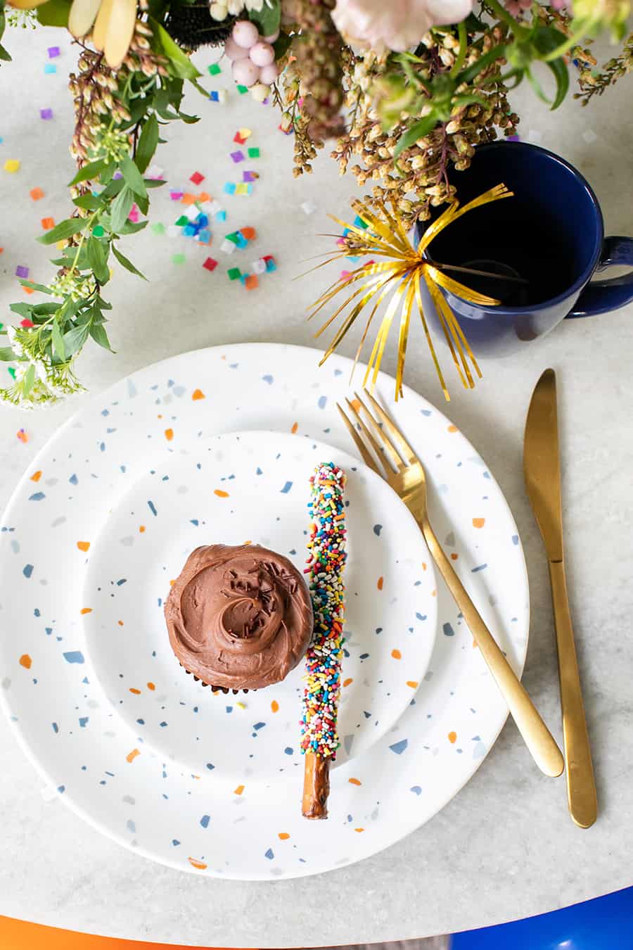 A birthday party set-up with flowers, cupcake, plates and confetti. 