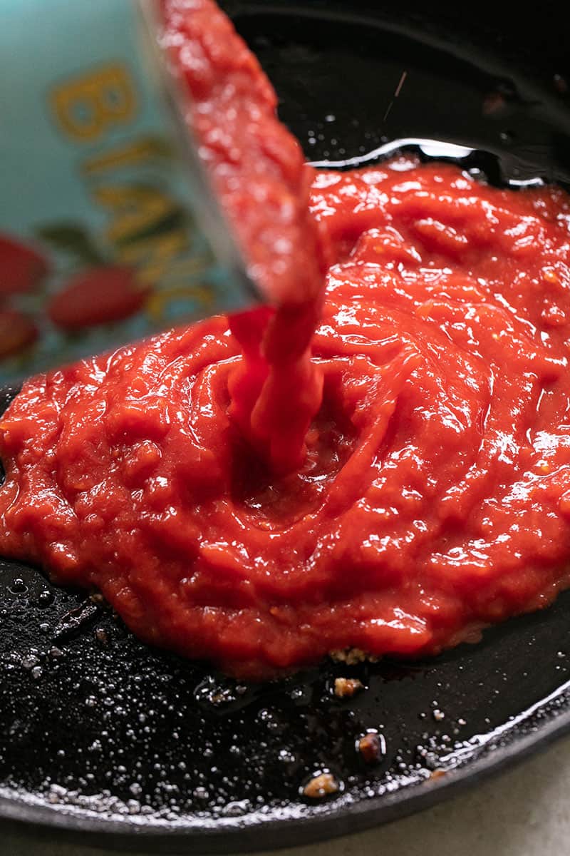 Can of tomatoes being poured into a cast iron pan. 