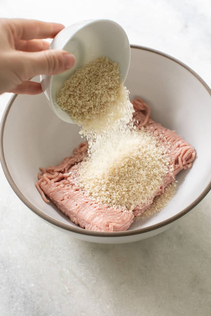 Pouring breadcrumbs into a bowl of turkey meat.