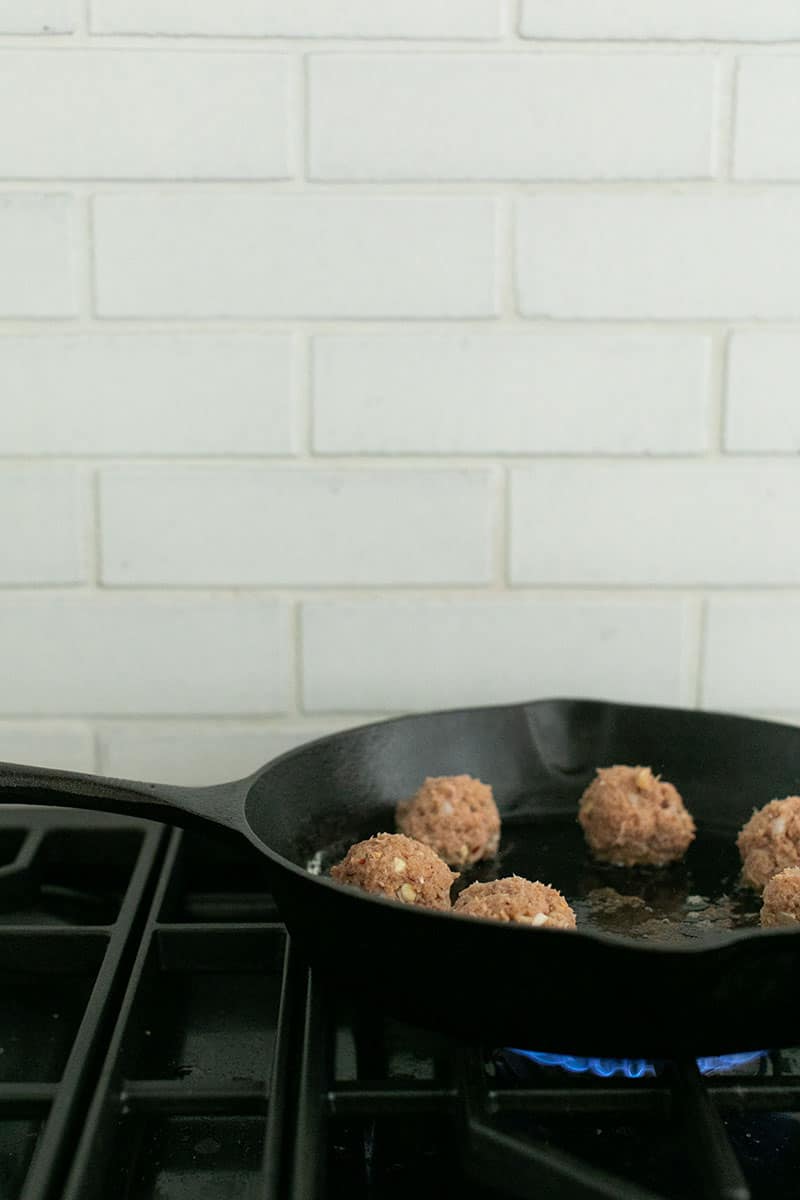 Turkey meatballs cooking in a cast iron pan on a stovetop. 