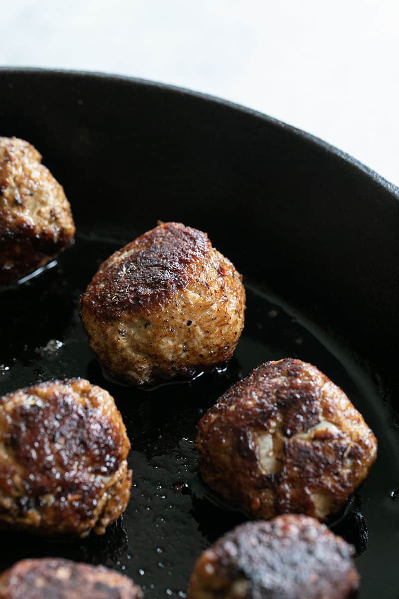 Golden brown turkey meatballs in a cast iron pan. 