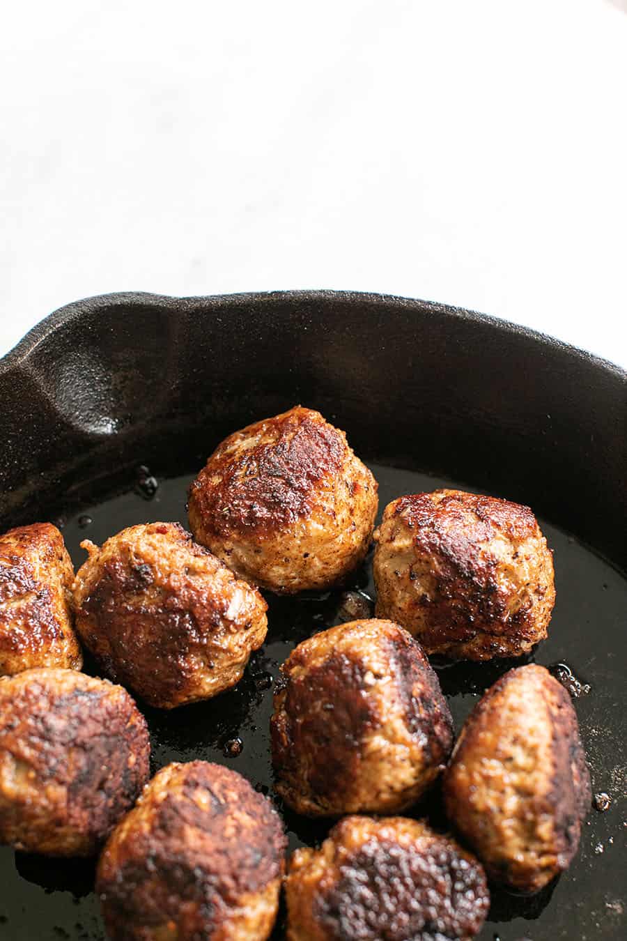 Golden brown meatballs in a cast iron pan. 