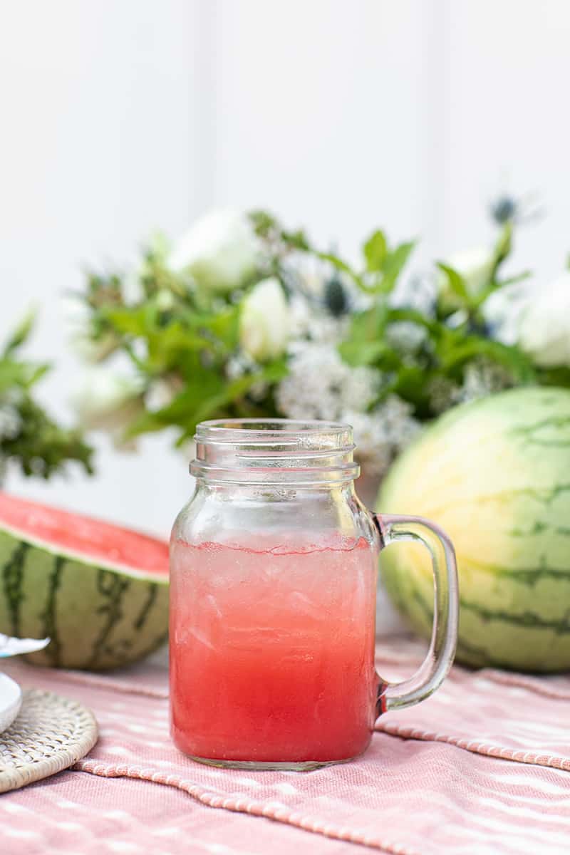 Glass mug filled with watermelon punch with watermelons in the background.