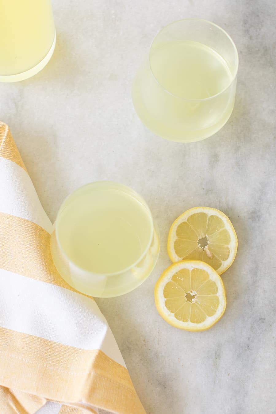 Two glasses of homemade Limoncello on a marble table with slices of lemon.