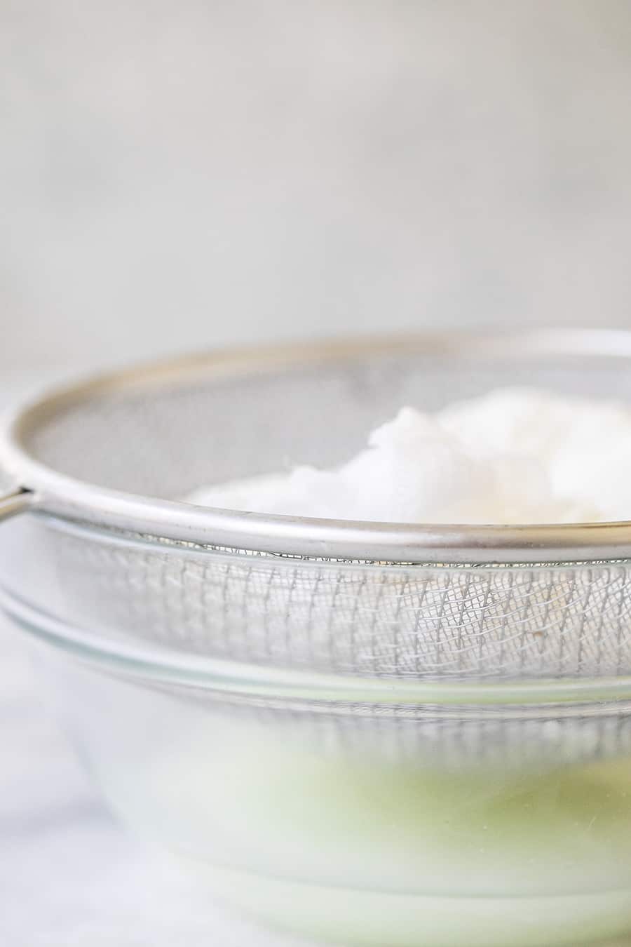 Whole milk yogurt being drained into a  clear bowl. 