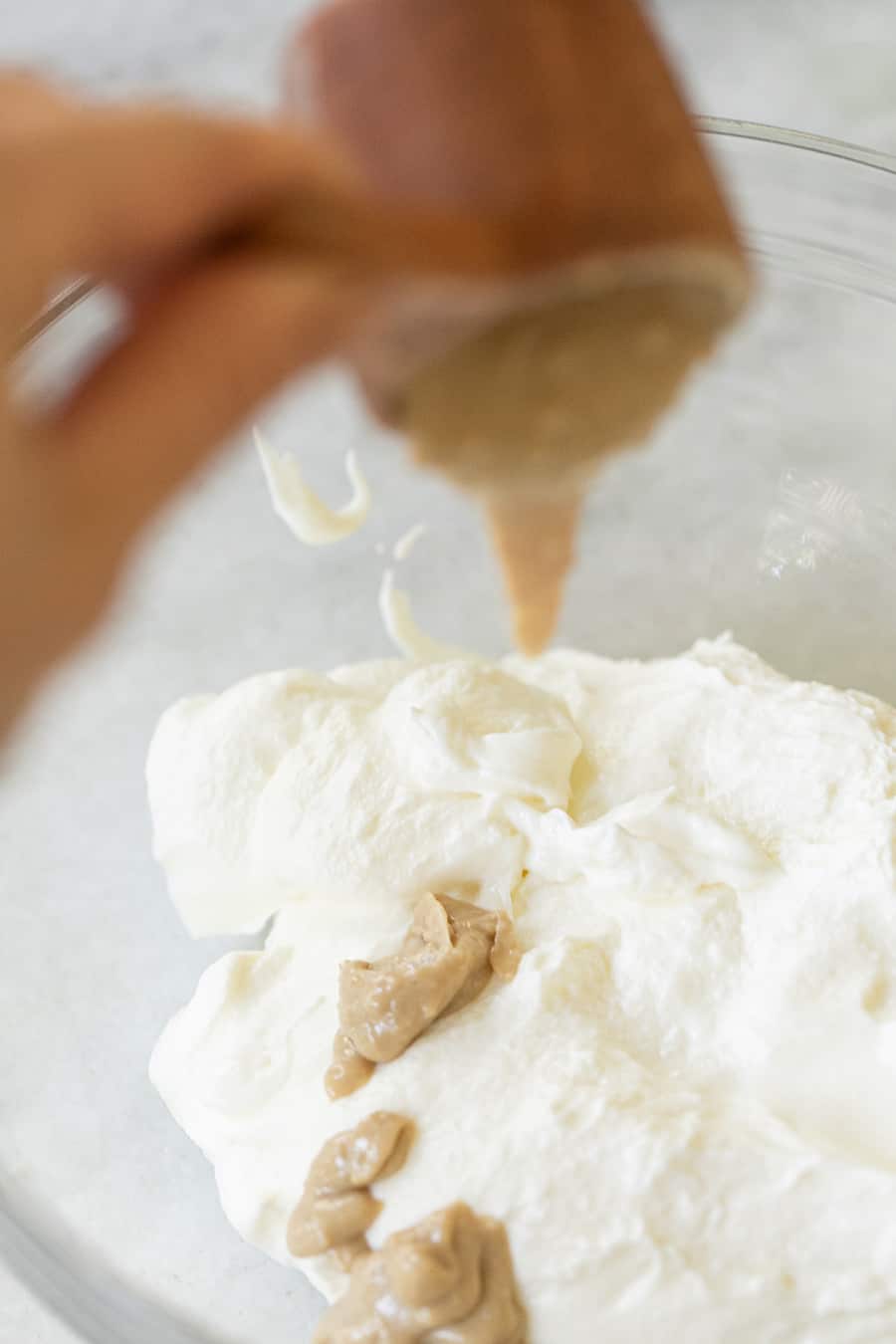 Tahini being poured into a bowl of yogurt.