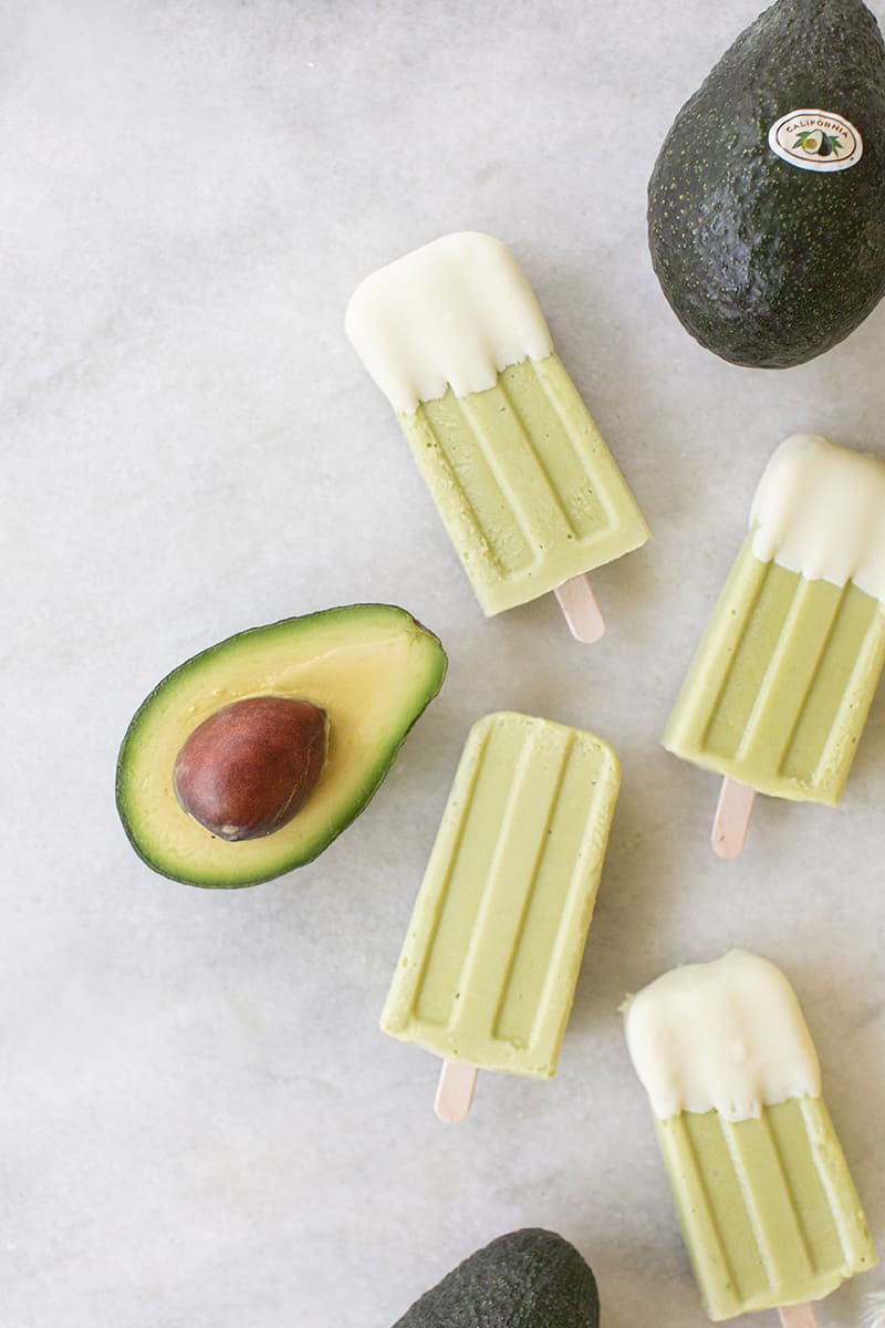 Green avocado popsicles on a marble table with an avocado cut in half.