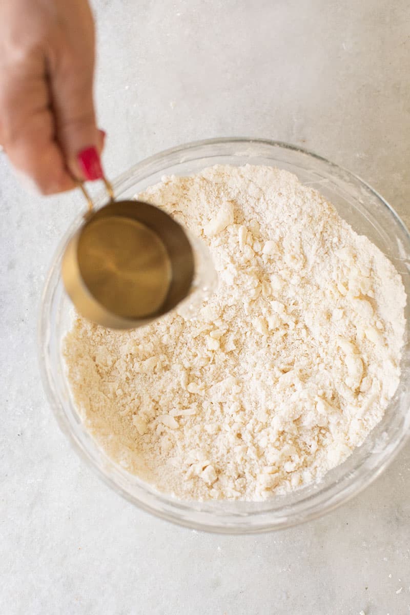 Hand pouring ice water into a bowl of pie crust