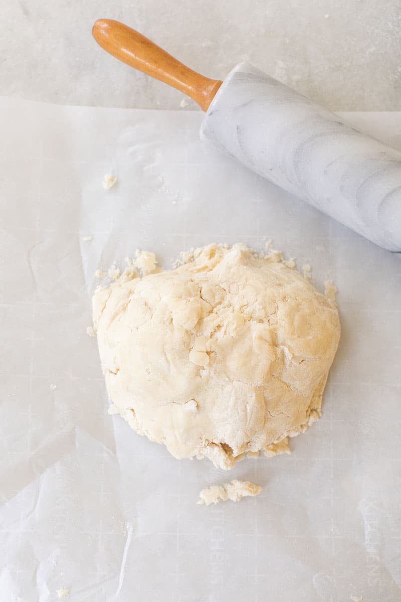 Pie dough in the form of a ball with a rolling pin on parchment paper.