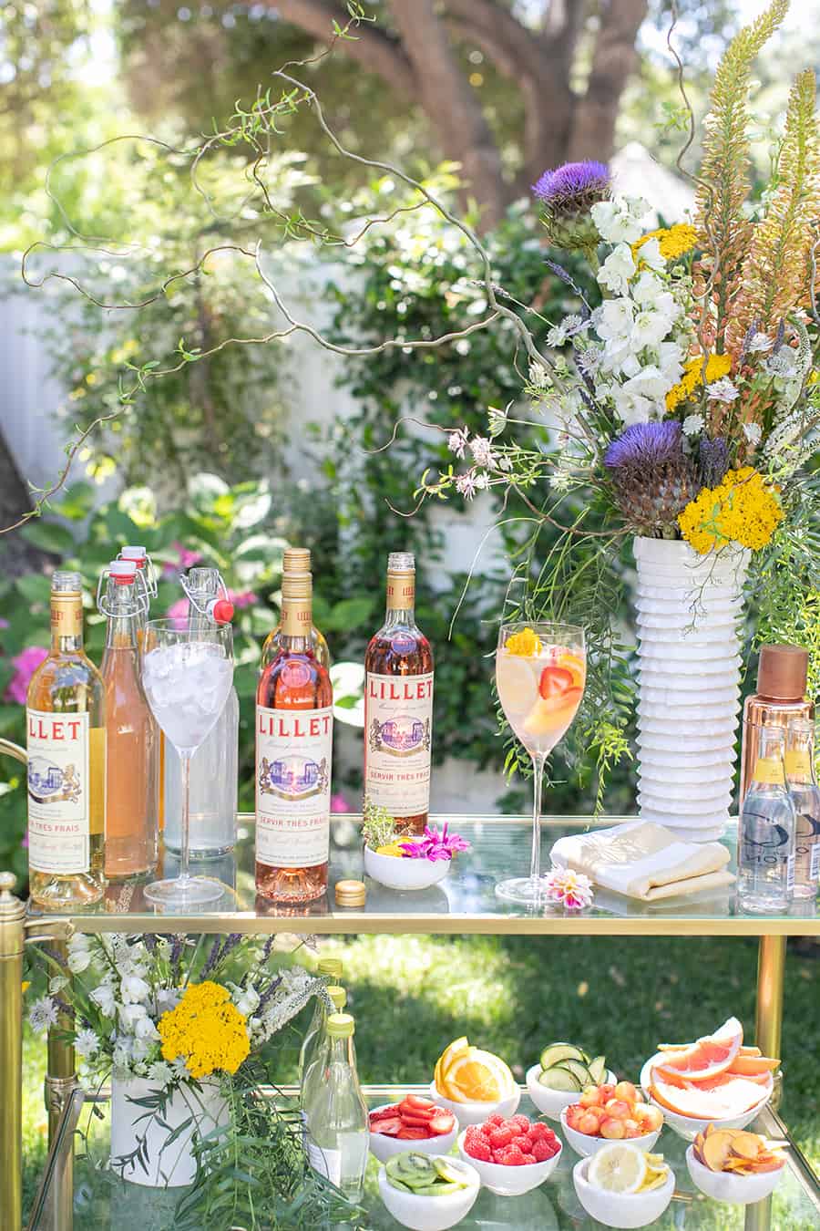 Bottles of Lillet on gold bar cart with flowers.