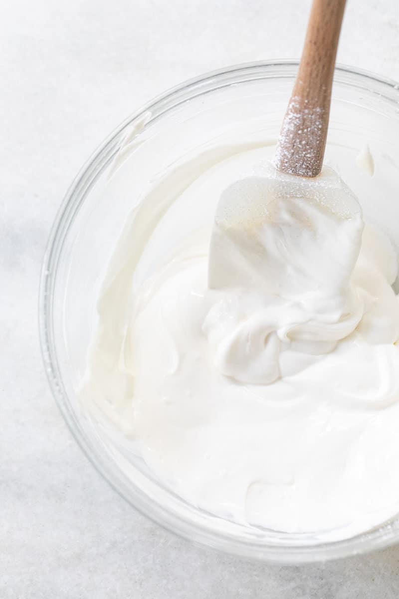 Whipped sour cream and sugar in a bowl with white spatula 