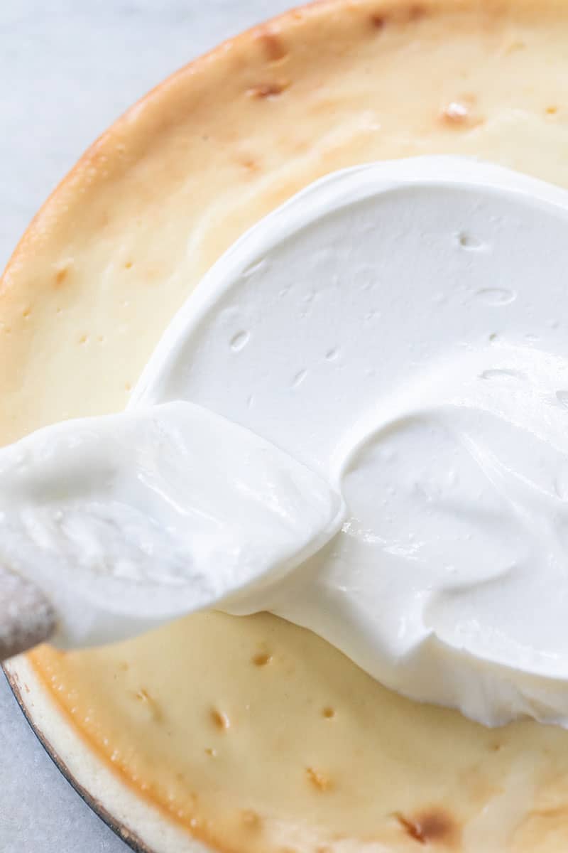 Whipped sour cream spread over cheesecake with spatula.