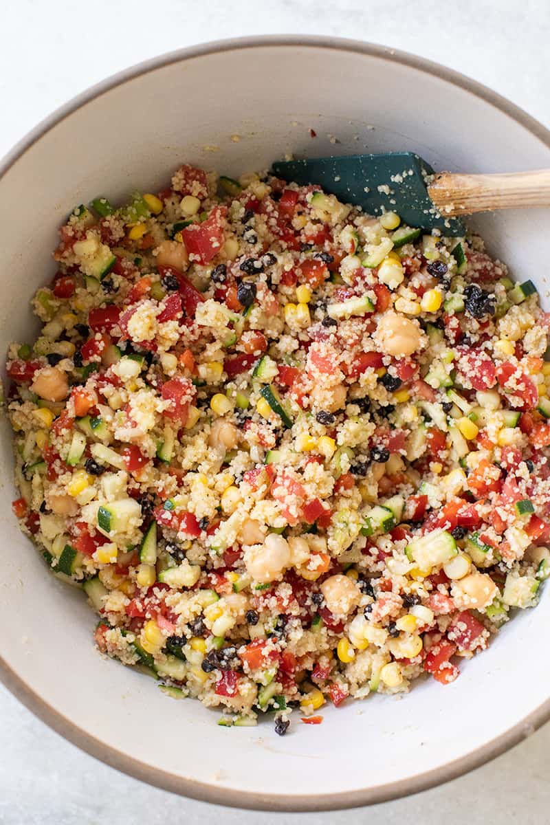 Summer couscous salad with vegetables in a bowl with a spatula. 