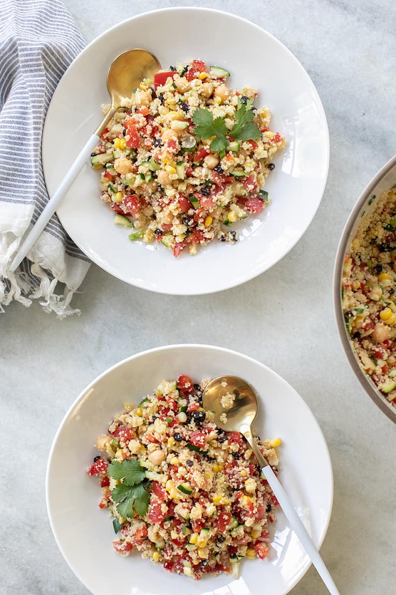 white bowl of couscous salad with gold spoon. 