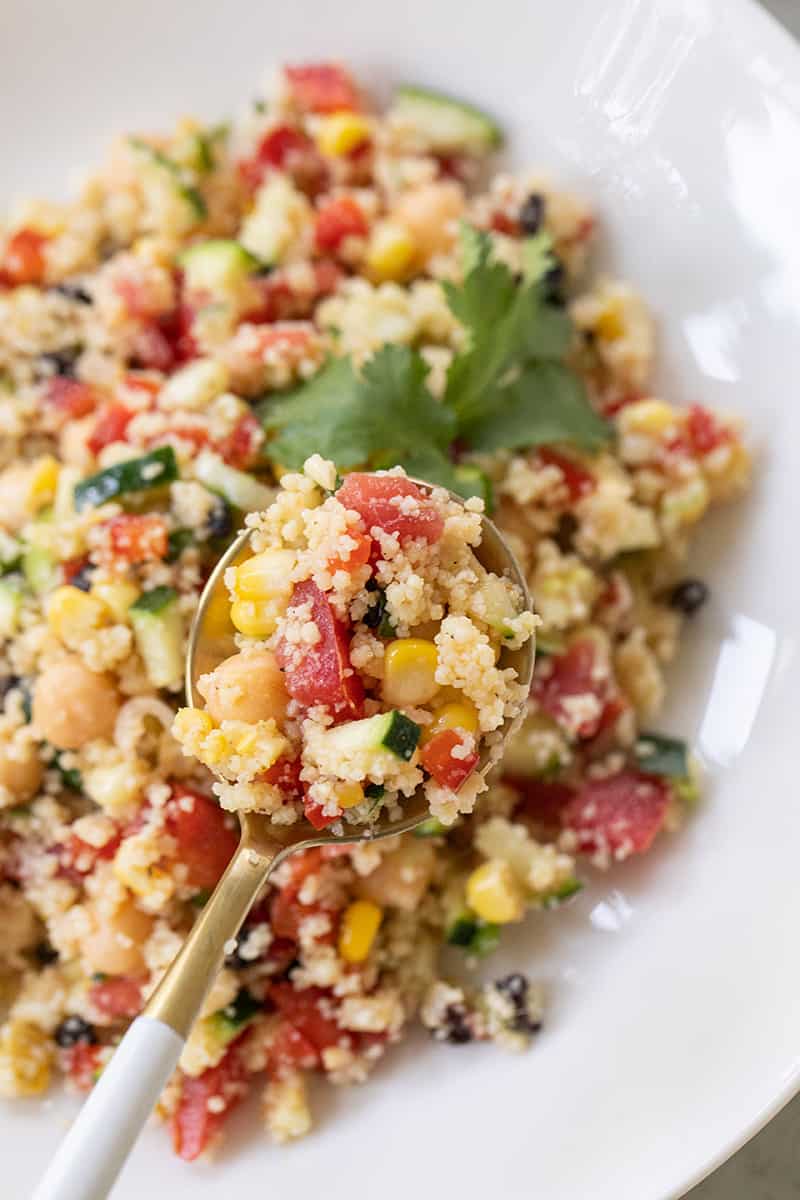 Summer couscous salad with fresh vegetables on a spoon.